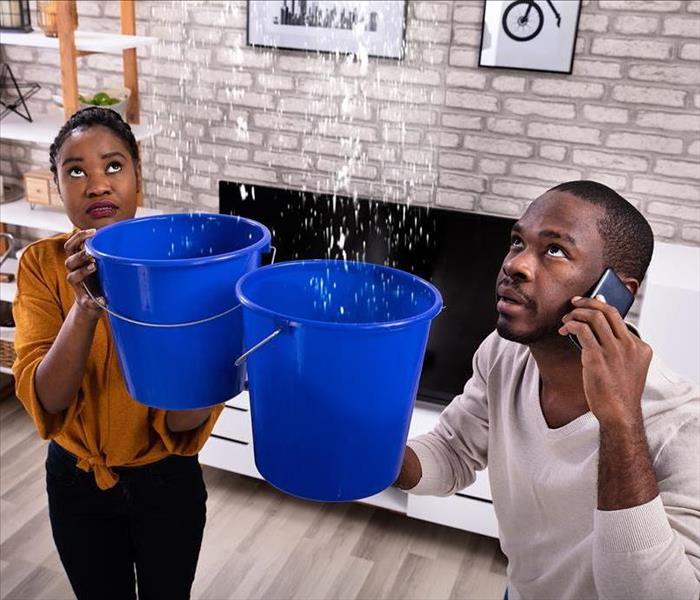 man and woman holding buckets under water damage leak